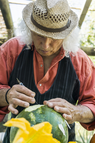 Älterer Mann bei der Arbeit an einer Wassermelone mit Schnitzwerkzeug, lizenzfreies Stockfoto