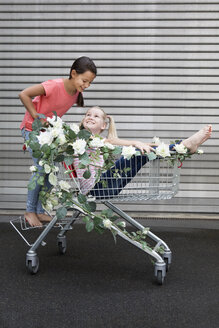 Zwei Mädchen spielen mit einem mit weißen Kunstblumen geschmückten Einkaufswagen - PSTF00173