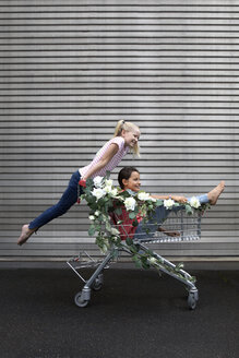 Zwei Mädchen spielen mit einem mit weißen Kunstblumen geschmückten Einkaufswagen - PSTF00179