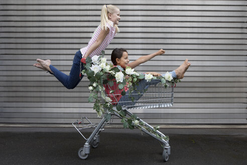 Zwei Mädchen spielen mit einem mit weißen Kunstblumen geschmückten Einkaufswagen - PSTF00180