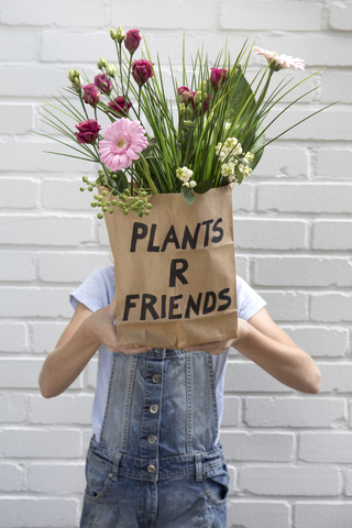 Mädchen versteckt Gesicht hinter Papiertüte mit Blumen, lizenzfreies Stockfoto