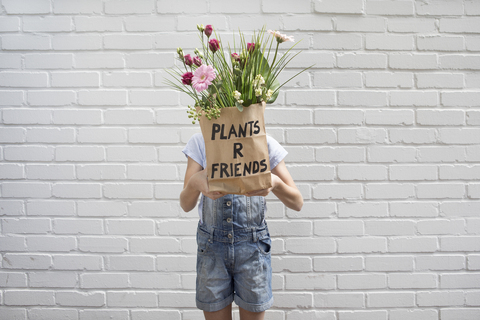 Girl hiding behind paper bag with flowers stock photo