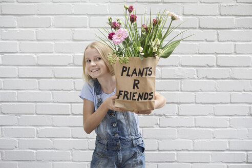 Porträt eines lächelnden Mädchens, das eine Papiertüte mit Blumen hält - PSTF00187