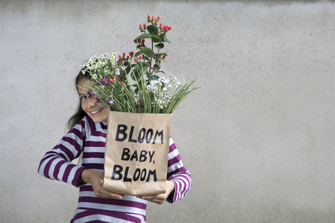 Lächelndes Mädchen hält Papiertüte mit Blumen, lizenzfreies Stockfoto