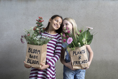 Porträt von zwei lächelnden Mädchen, die Papiertüten mit Blumen halten - PSTF00194