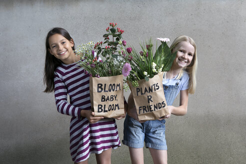 Porträt von zwei lächelnden Mädchen, die Papiertüten mit Blumen halten - PSTF00195