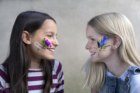 Zwei lächelnde Mädchen mit Blumenköpfen auf ihren Wangen, lizenzfreies Stockfoto