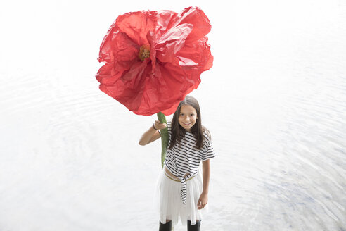 Porträt eines lächelnden Mädchens, das in einem See steht und eine übergroße rote Kunstblume hält - PSTF00204