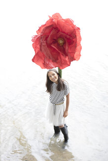 Porträt eines lächelnden Mädchens, das mit einer übergroßen roten Kunstblume in einem See steht - PSTF00207