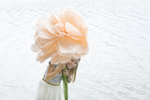 Porträt eines lächelnden blonden Mädchens, das in einem See steht und eine übergroße Kunstblume hält - PSTF00208