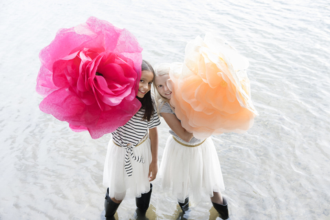 Zwei Mädchen stehen in einem See mit zwei übergroßen Kunstblumen, lizenzfreies Stockfoto