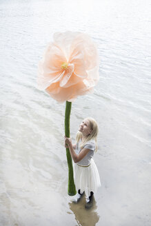 Lächelndes blondes Mädchen, das in einem See steht und eine übergroße Kunstblume hält - PSTF00211
