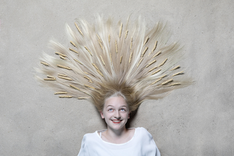 Portrait of smiling girl lying on floor with ears of wheat on hair looking up stock photo