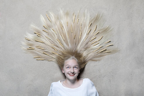 Porträt eines lächelnden Mädchens, das auf dem Boden liegt und mit Weizenähren im Haar nach oben schaut - PSTF00223
