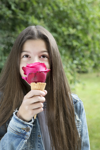 Girl smelling pink rose blossom in ice cream cone stock photo