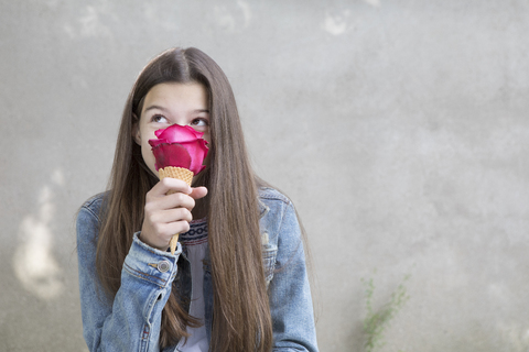 Mädchen riecht an einer rosa Rosenblüte in einer Eistüte mit, lizenzfreies Stockfoto