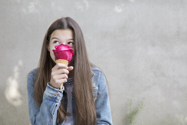 Mädchen riecht an einer rosa Rosenblüte in einer Eistüte mit - PSTF00227