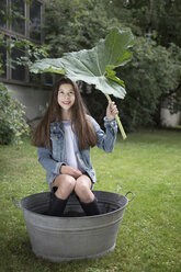 Porträt eines lächelnden Mädchens, das unter einer großen Wanne im Garten sitzt - PSTF00230