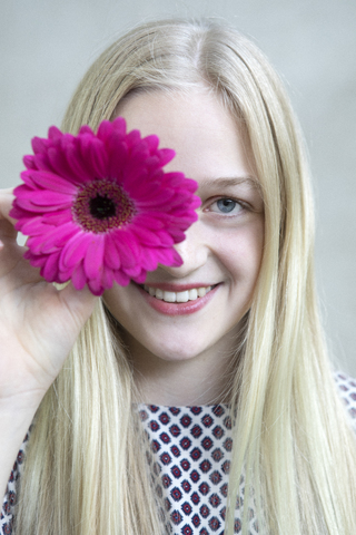Porträt eines lächelnden blonden Mädchens mit einem Blumenkopf aus rosa Gerbera, lizenzfreies Stockfoto