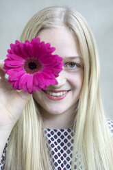 Porträt eines lächelnden blonden Mädchens mit einem Blumenkopf aus rosa Gerbera - PSTF00232