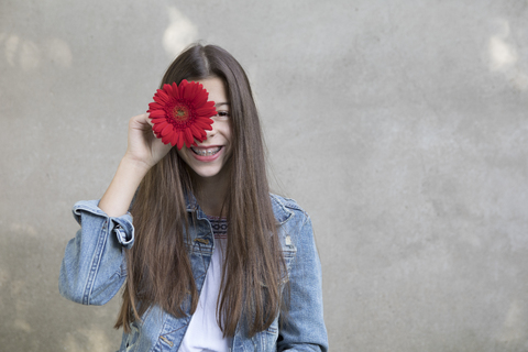 Porträt eines lachenden Mädchens mit einem Blumenkopf aus roter Gerbera, lizenzfreies Stockfoto