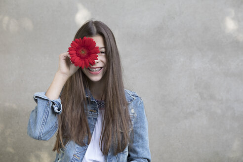 Porträt eines lachenden Mädchens mit einem Blumenkopf aus roter Gerbera - PSTF00235