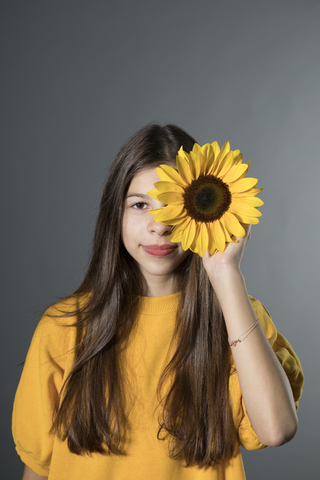 Porträt eines lächelnden Mädchens mit Sonnenblume vor einem grauen Hintergrund, lizenzfreies Stockfoto