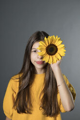 Porträt eines lächelnden Mädchens mit Sonnenblume vor einem grauen Hintergrund - PSTF00239