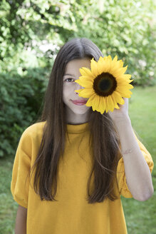 Porträt eines lächelnden Mädchens mit Sonnenblume im Garten - PSTF00240