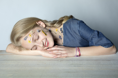 Porträt eines lächelnden blonden Mädchens mit einer Tätowierung aus gepressten Blumen im Gesicht, lizenzfreies Stockfoto