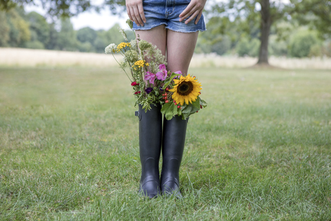 Beine eines Mädchens, das auf einer Wiese mit Blumensträußen in ihren Gummistiefeln steht, lizenzfreies Stockfoto