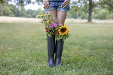 Beine eines Mädchens, das auf einer Wiese mit Blumensträußen in ihren Gummistiefeln steht - PSTF00253