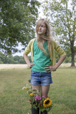 Porträt eines blonden Mädchens, das auf einer Wiese mit Blumensträußen in ihren Gummistiefeln steht, lizenzfreies Stockfoto