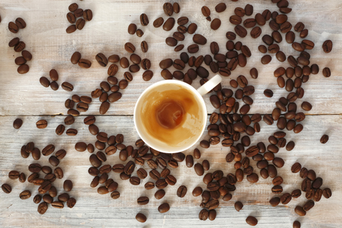 Leere Tasse mit Resten von Espresso und gerösteten Kaffeebohnen auf Holz, lizenzfreies Stockfoto