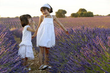 Zwei Mädchen im weißen Kleid spielen auf dem Feld der lila Blumen - AURF05654