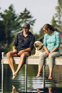 Woman, dog and man relaxing on the end of long lake dock. - AURF05777