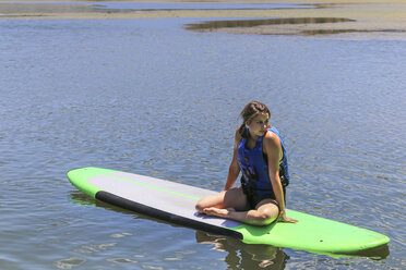 Junge Frau sitzt auf einem Paddleboard auf einem ruhigen See - AURF05784