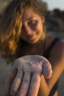 Frau am Strand, die eine kleine Krabbe auf einer mit Sand bedeckten Hand zeigt - AURF05838