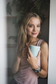 Porträt einer lächelnden blonden jungen Frau mit Kaffeetasse - KKAF01987