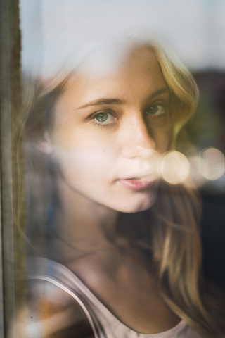 Porträt einer jungen Frau hinter einer Fensterscheibe, lizenzfreies Stockfoto