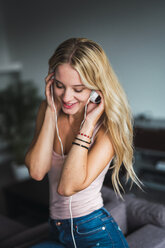 Smiling young woman listening to music with headphones at home - KKAF02006