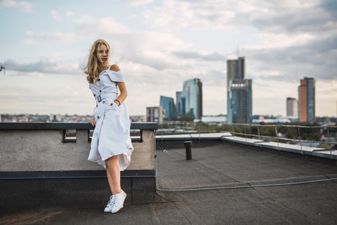 Blonde junge Frau im weißen Kleid auf der Dachterrasse stehend, lizenzfreies Stockfoto