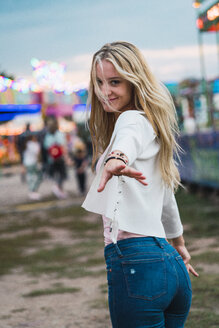 Smiling young woman on a funfair reaching out her hand - KKAF02021
