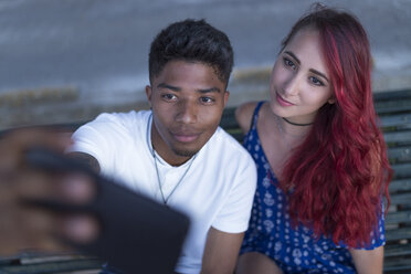 Porträt eines jungen Paares, das zusammen auf einer Bank sitzt und ein Selfie mit seinem Smartphone macht - JPTF00005