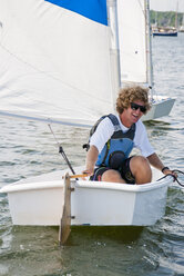 Ein Mann sitzt lachend in einem kleinen Segelboot während eines Sommer-Segelcamps - AURF05865