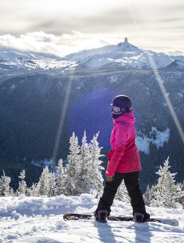 Eine Snowboarderin macht eine Pause und blickt auf die Aussicht auf Black Tusk vom Whistler Blackcomb Ski Resort hinaus, lizenzfreies Stockfoto