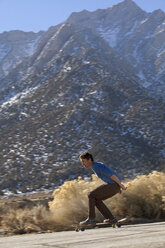 Erwachsener Mann auf dem Skateboard am Fuße der Berge in der Sierra Nevada - AURF05935