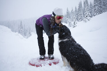 Adult woman petting dog in snowy mountains, Sandpoint, Idaho, USA - AURF05936