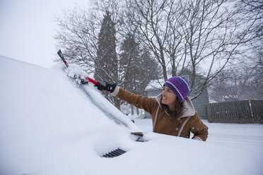 Eine erwachsene Frau, die ihre Windschutzscheibe nach einer frischen Schneedecke abräumt - AURF05985