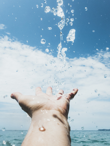 Nahaufnahme der Hand einer Frau im Meer und Wassertropfen, lizenzfreies Stockfoto